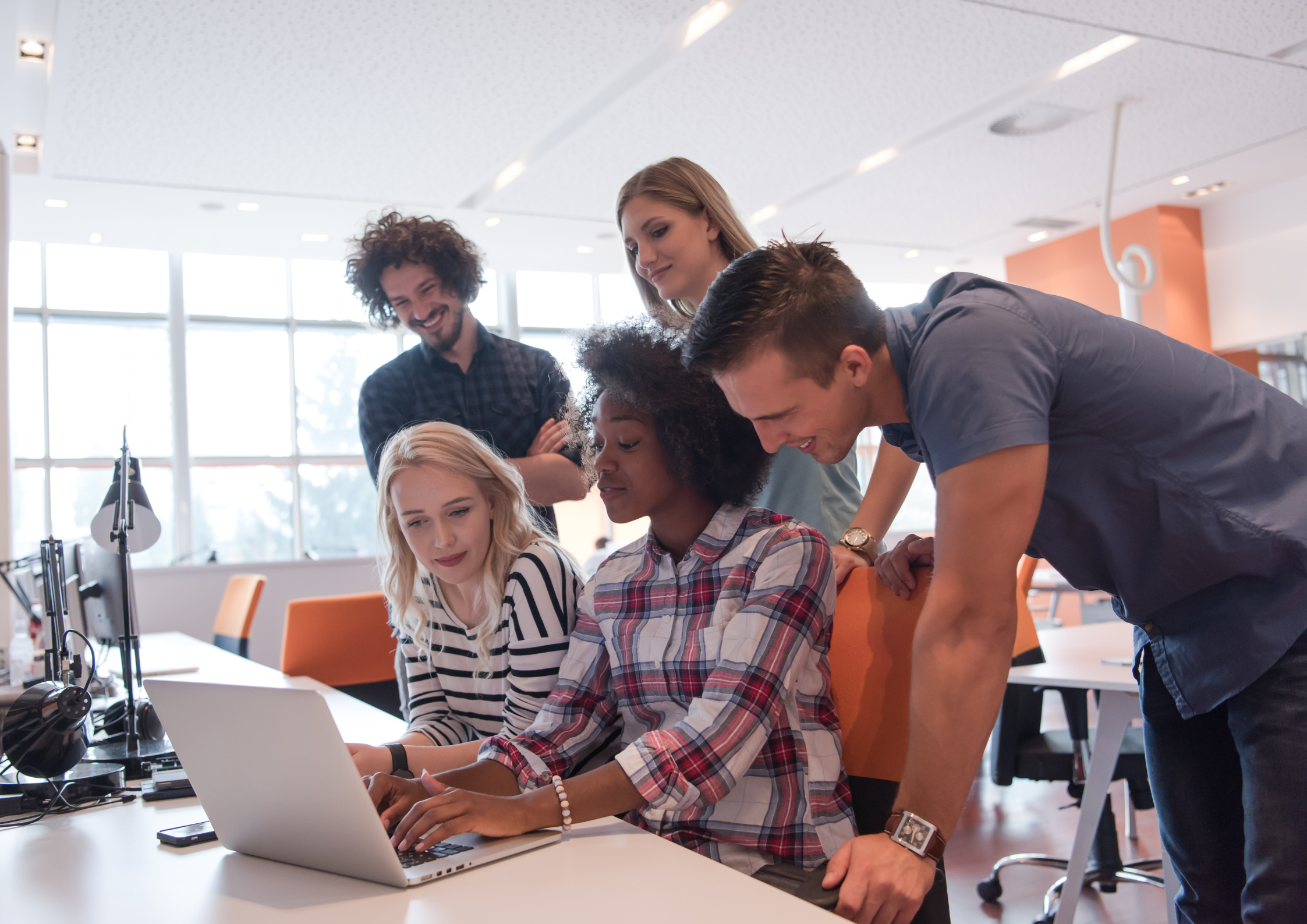 Group of casually dressed people in an office space looking at a computer