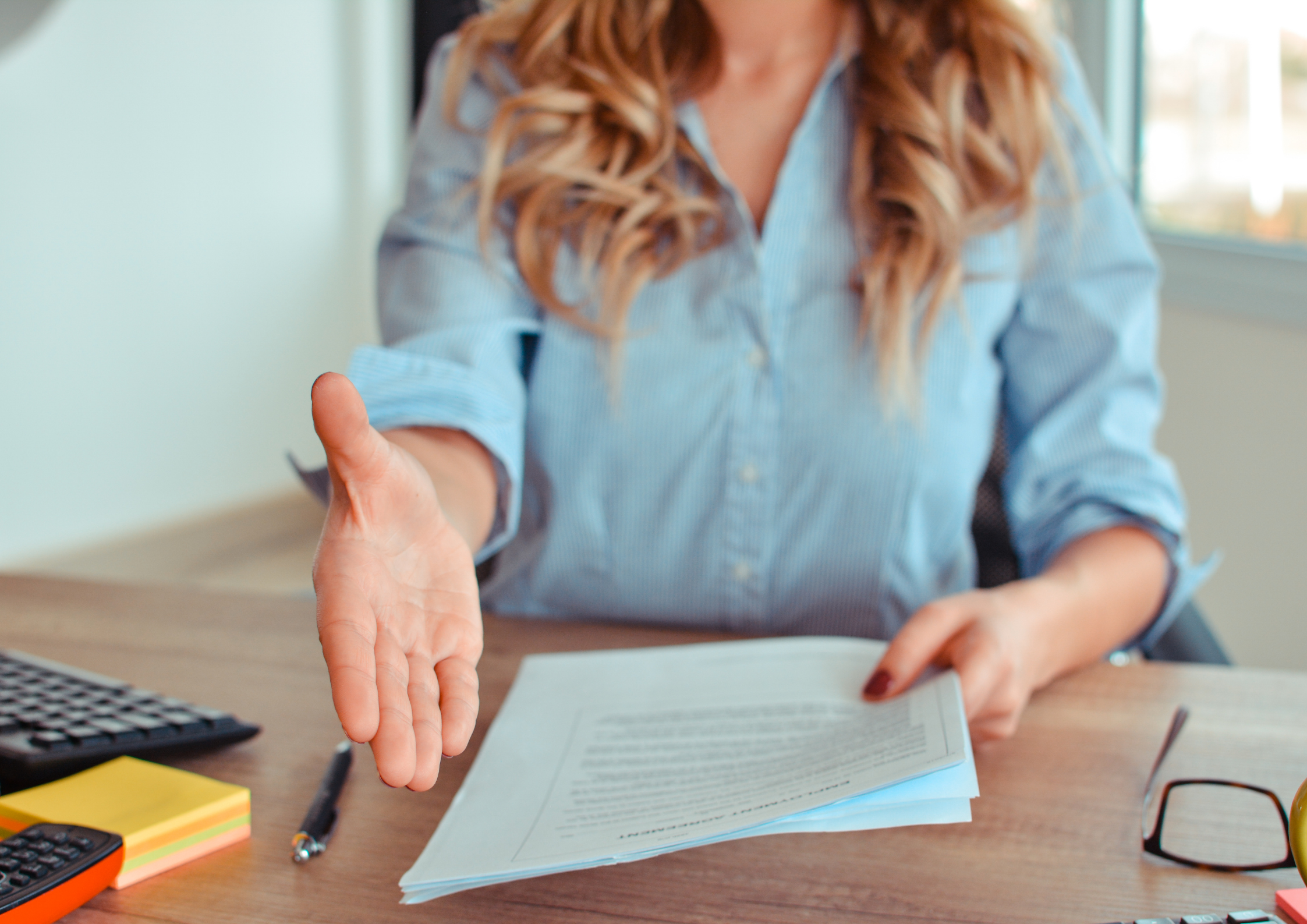 person extending their hand, with a job offer laying on the desk