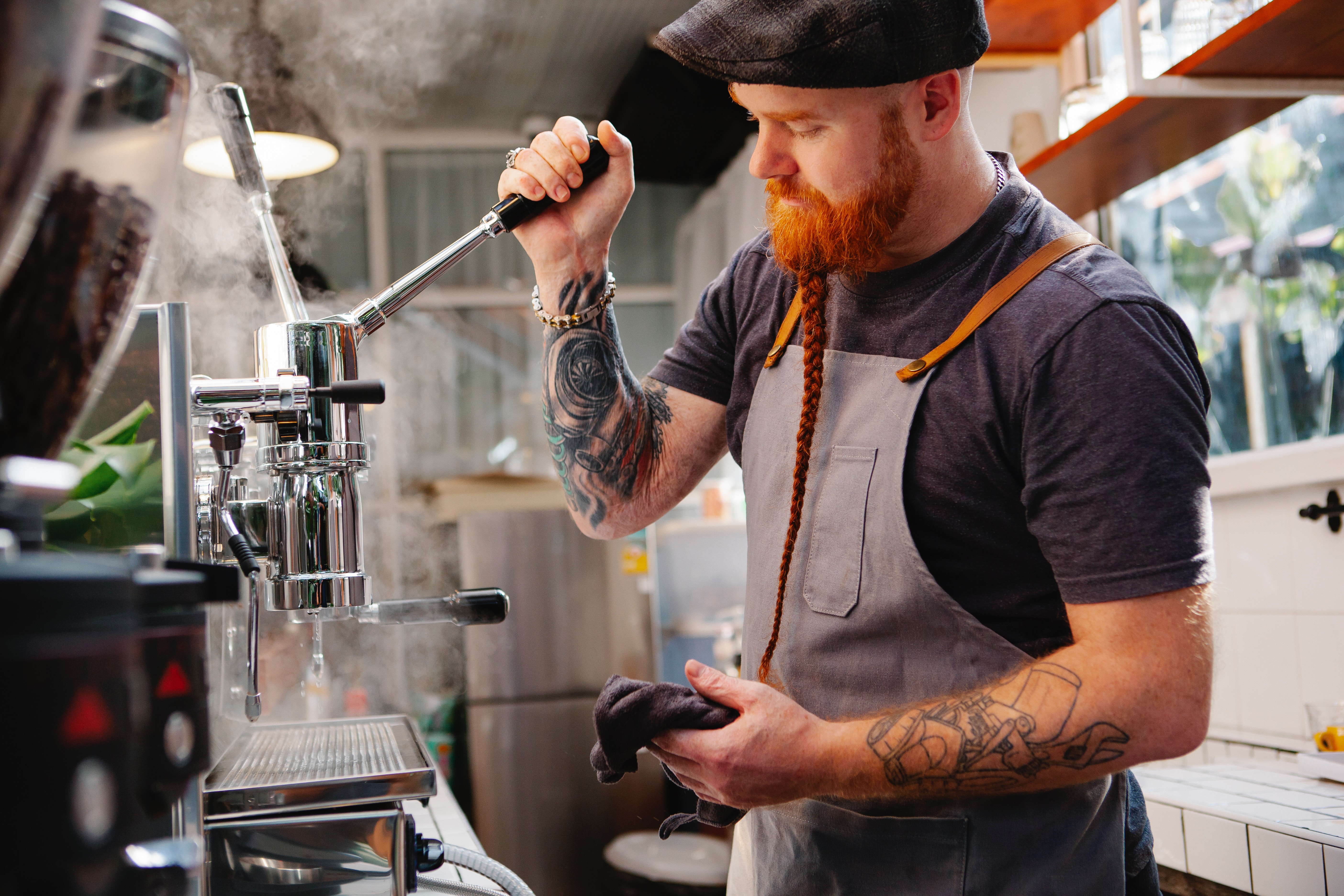 Male barista with ginger hair and long plaited beard making a coffee